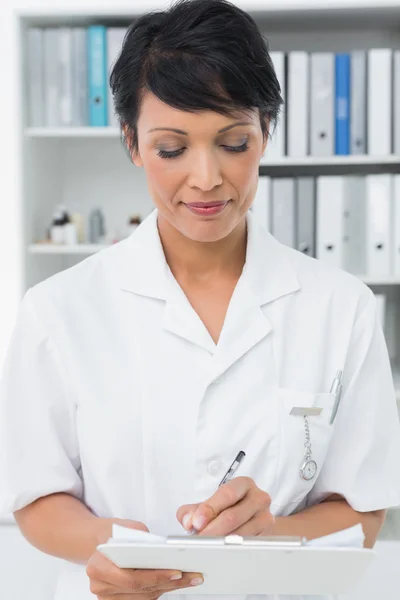 Concentrated female doctor writing on clipboard — Stock Photo, Image