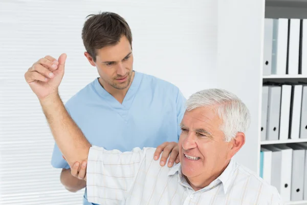 Physiotherapist assisting senior man to stretch his hand — Stock Photo, Image