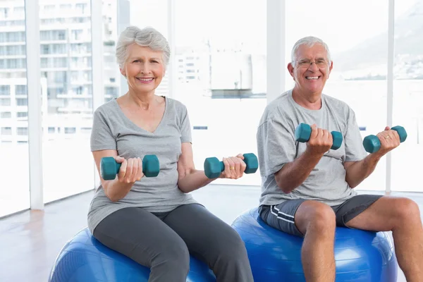 Senior couple sitting on fitness balls with dumbbells — Stock Photo, Image