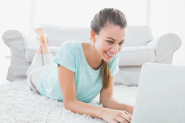 Mulher feliz deitada no tapete usando seu laptop — Fotografia de Stock