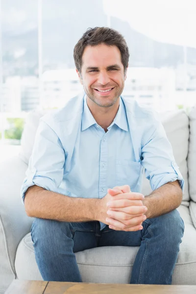 Homem atraente sentado no sofá sorrindo para a câmera — Fotografia de Stock