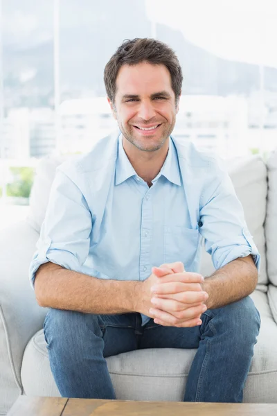 Homme attrayant assis sur le canapé souriant à la caméra — Photo