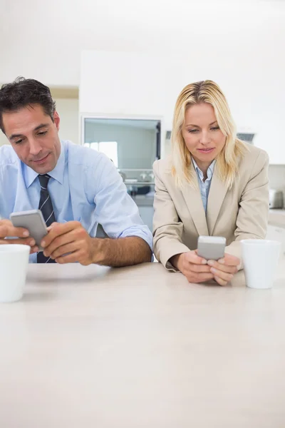 Couple text messaging in kitchen — Stock Photo, Image