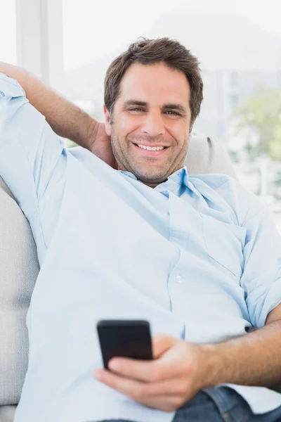 Lächelnder Mann, der auf dem Sofa sitzt und auf seinem Handy SMS schreibt — Stockfoto