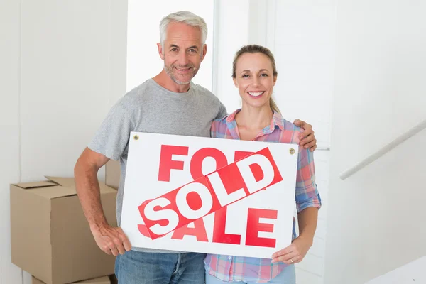 Feliz pareja de pie y sosteniendo letrero vendido — Foto de Stock