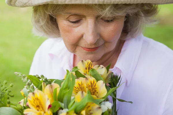 Starsza kobieta, pachnące kwiaty — Zdjęcie stockowe