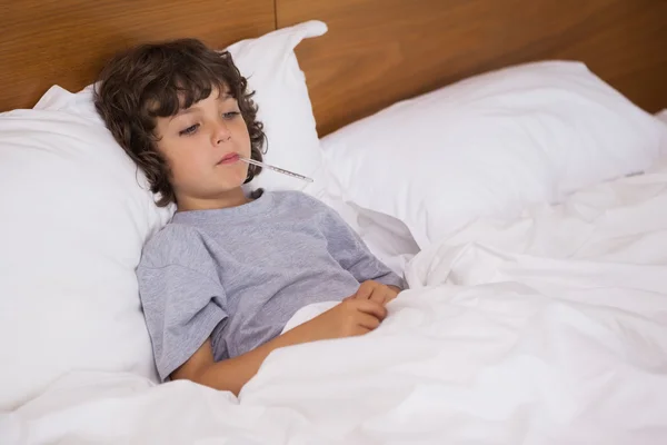 Niño enfermo con termómetro descansando en la cama — Foto de Stock