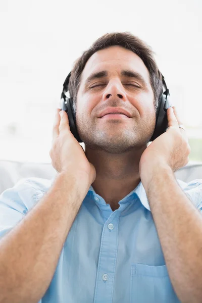 Hombre contento sentado en el sofá escuchando música con los ojos cerrados — Foto de Stock