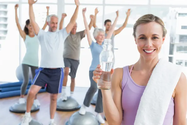 Kvinna med flaska med människor som sträcker händerna på fitnesstudio — Stockfoto