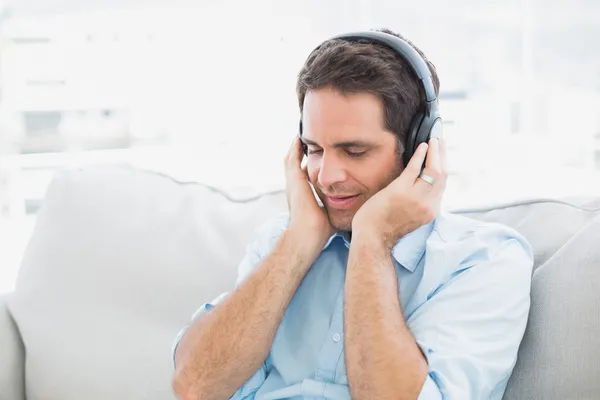 Bonito homem sentado no sofá ouvindo música — Fotografia de Stock