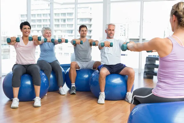 Lezione di fitness con manubri seduti su palle da ginnastica in una palestra luminosa — Foto Stock