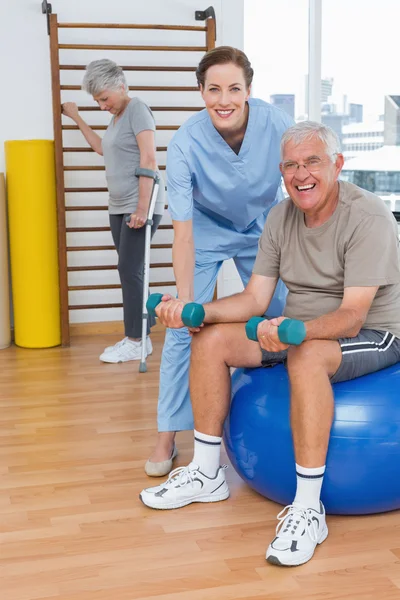 Therapist assisting senior man with dumbbells — Stock Photo, Image