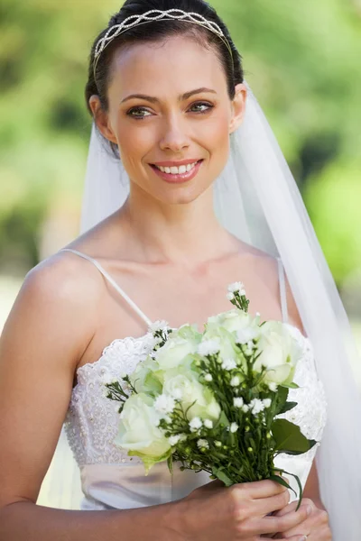 Souriant jeune belle mariée avec bouquet dans le parc — Photo