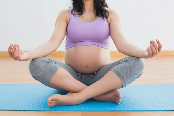 Zwangere brunette zittend op mat in lotus pose — Stockfoto