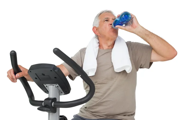 Senior man drinkwater op upright bike — Stockfoto