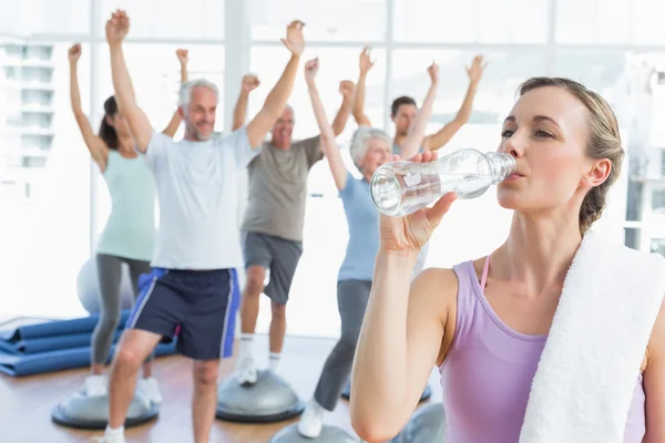 Mujer bebiendo agua con la gente estirando las manos en el gimnasio —  Fotos de Stock