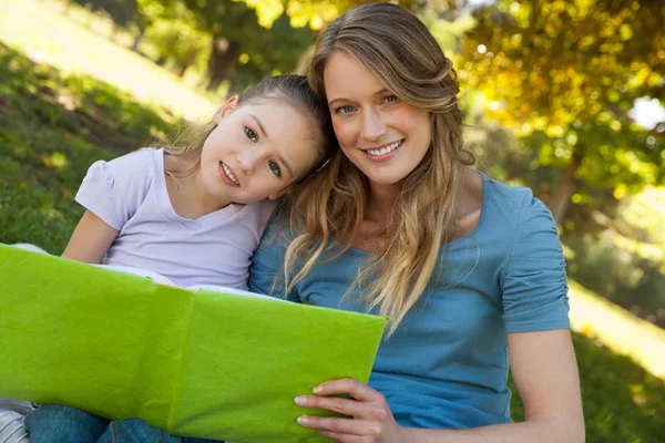 Lycklig mor och dotter läser en bok på park — Stockfoto