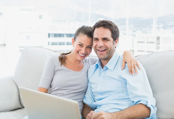 Счастливая пара, сидящая на диване с ноутбуком вместе — стоковое фото