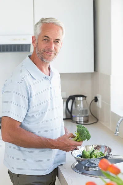 Casual man rinsing broccoli in colander and smiling at camera — Stock Photo, Image