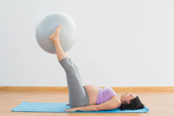 Happy pregnant woman lifting exercise ball with legs — Stock Photo, Image