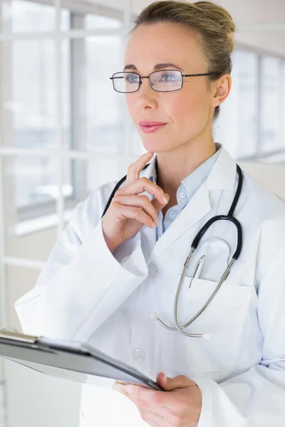 Thoughtful female doctor with clipboard in hospital — Stock Photo, Image