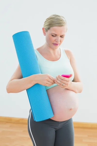 Pregnant woman holding exercise mat sending a text message — Stock Photo, Image
