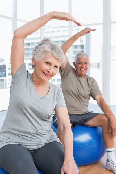 Casal sênior fazendo exercícios de alongamento em bolas de fitness — Fotografia de Stock