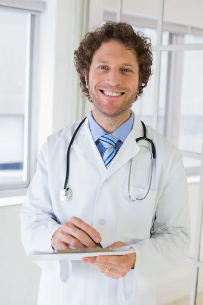 Happy male doctor with clipboard in hospital — Stock Photo, Image