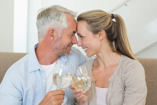 Happy couple sitting on couch toasting with white wine — Stock Photo, Image