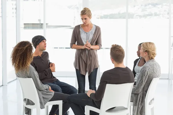 Rehab group listening to woman standing up introducing herself — Stock Photo, Image