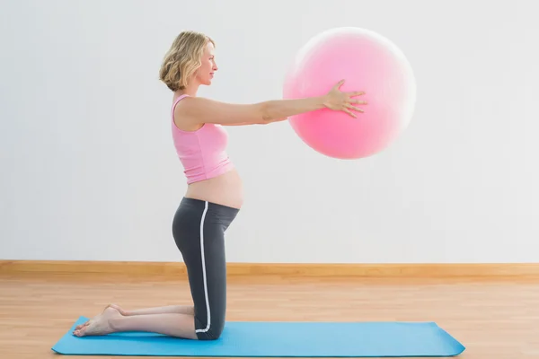 Mulher grávida loira alegre levantando bola de exercício — Fotografia de Stock