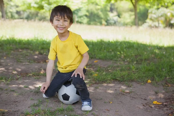 Portrait of a cute boy sitting on football at park — Stock Photo, Image