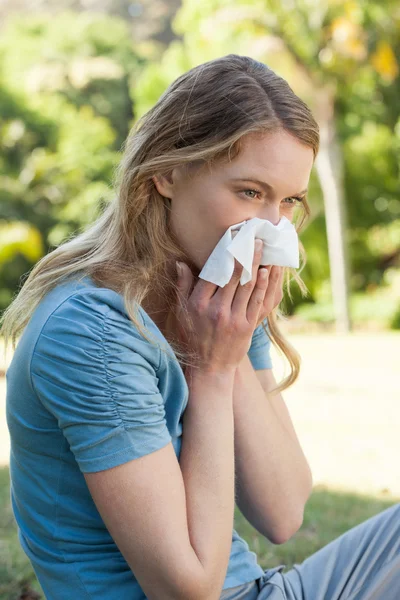 Woman blowing nose with tissue paper at park — Stock Photo, Image