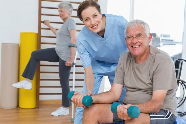 Therapist assisting senior man with dumbbells — Stock Photo, Image