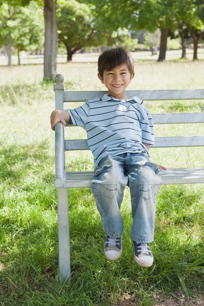 Portrait of a happy boy sitting on bench at park — Stock Photo, Image