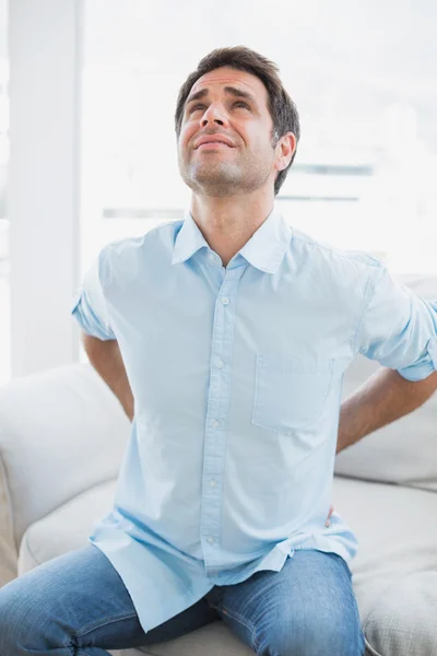 Handsome man sitting on sofa stretching painful back — Stock Photo, Image