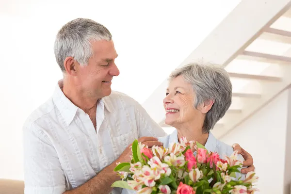 Senior koppel glimlachen bij elkaar houden boeket van bloemen — Stockfoto