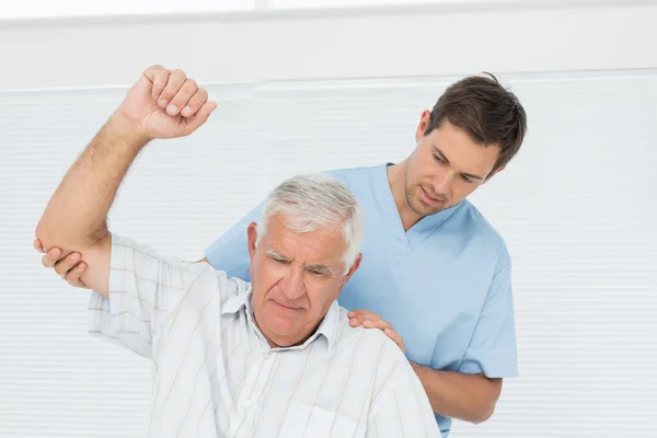 Fisioterapeuta masculino que ayuda al hombre mayor a levantar la mano —  Fotos de Stock