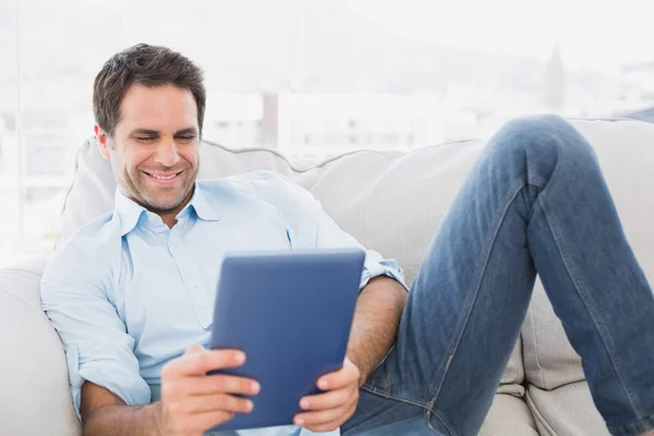 Smiling man relaxing on the couch using his tablet — Stock Photo, Image