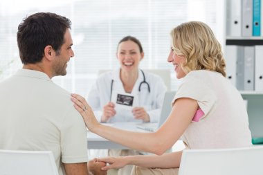 Expectant couple with doctor in clinic clipart
