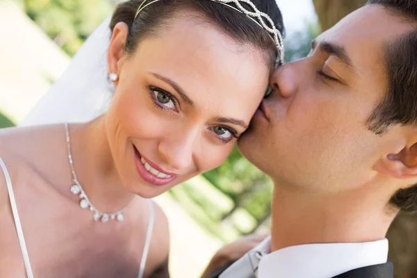 Bride being kissed by groom in garden — Stock Photo, Image