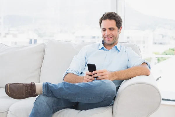 Homem alegre sentado no sofá usando seu smartphone — Fotografia de Stock