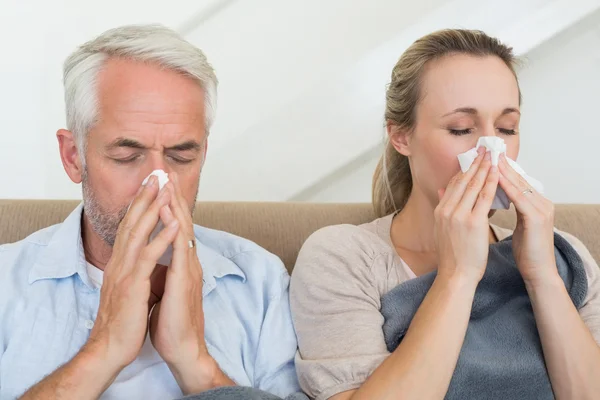 Sick couple blowing their noses sitting on the couch — Stock Photo, Image