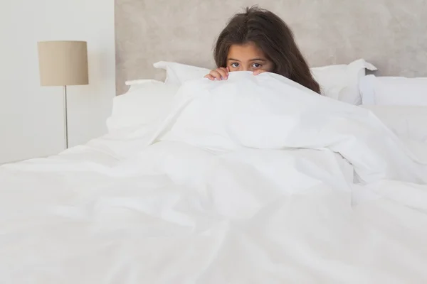 Menina escondendo rosto atrás de lençol na cama — Fotografia de Stock