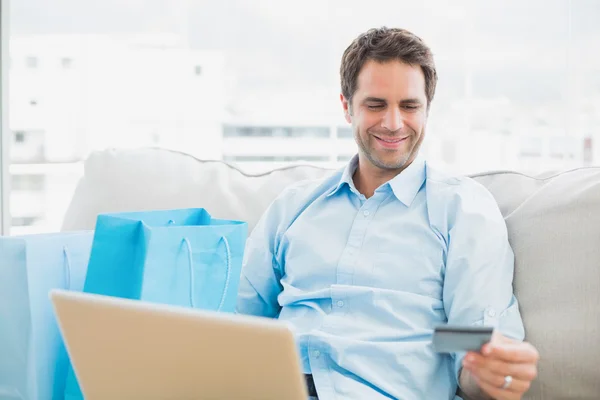Bel homme en utilisant ordinateur portable assis sur canapé shopping en ligne — Photo