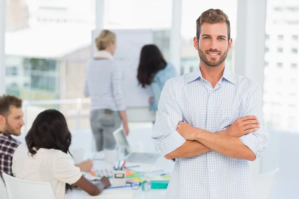 Handsome man smiling at camera while his colleagues are working — Stock Photo, Image