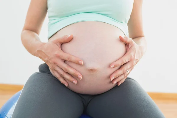 Беременная женщина сидит на мяче для упражнений, держа живот. — стоковое фото