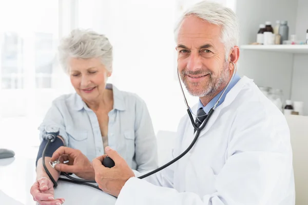 Доктор измеряет кровяное давление своего пациента на пенсии — стоковое фото