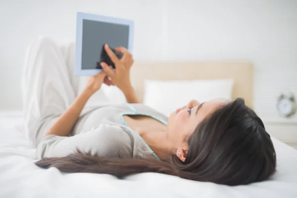 Chica acostada en la cama mirando a su PC tableta — Foto de Stock