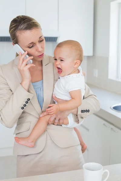 Empresaria sosteniendo a su bebé llorando hablando por teléfono —  Fotos de Stock